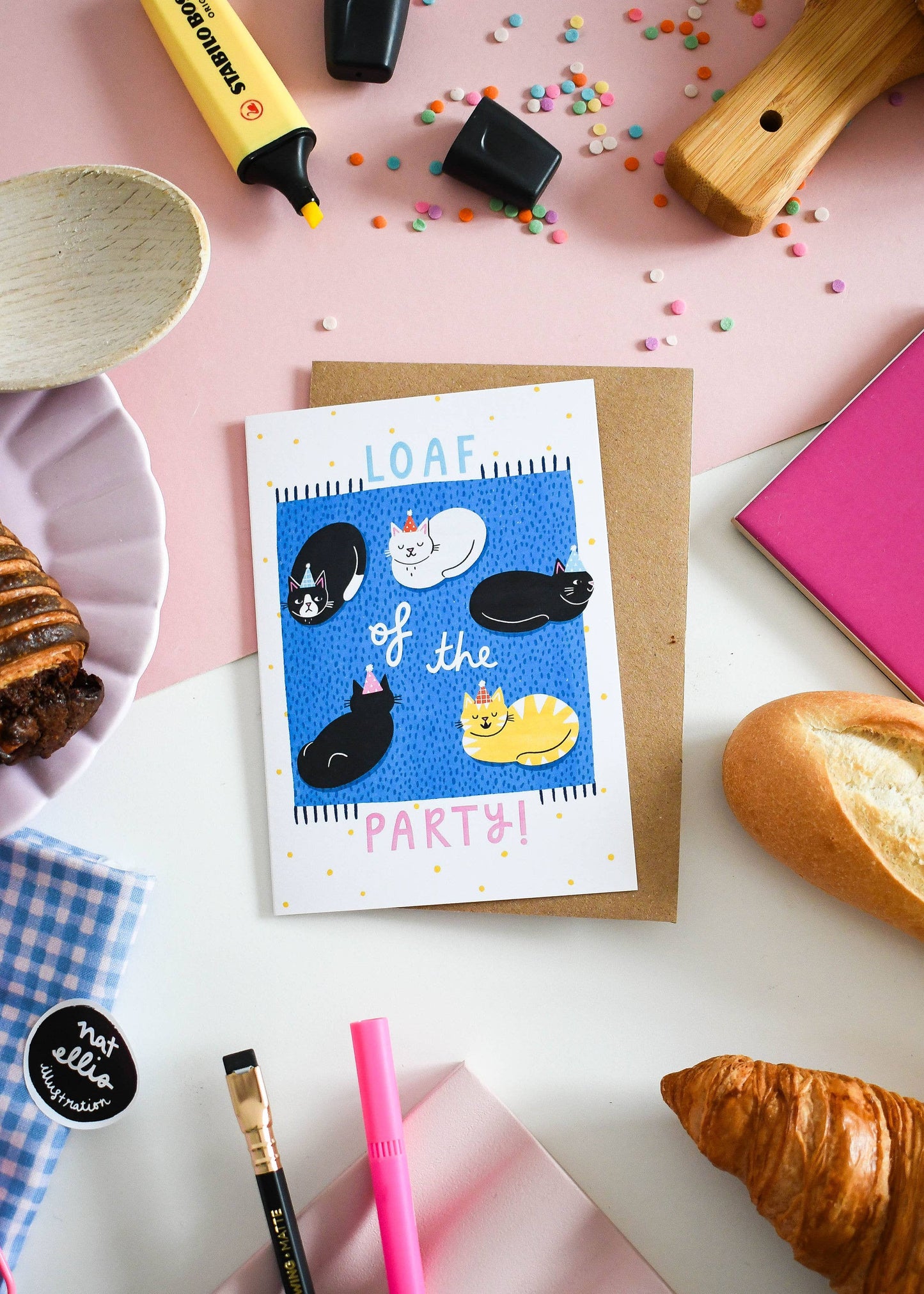 Greeting card with cat illustrations on a table with bread and stationery items