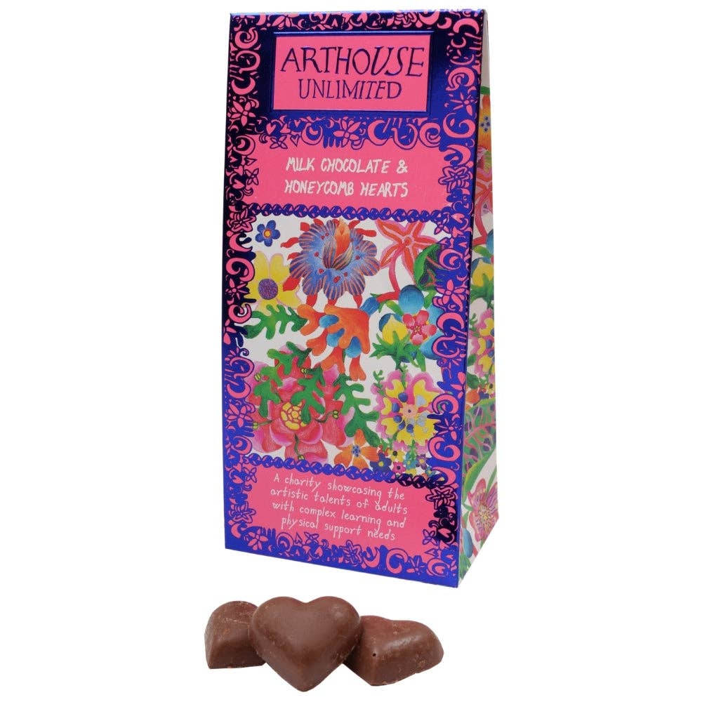 A tall decorative chocolate box with a bright floral and ornamental print in pink, purple, blue, green, and yellow, with three milk chocolate heart-shaped chocolates placed in front on a white background. The box reads 'ARTHHOUSE UNLIMITED' and 'MILK CHOCOLATE & HOME MADE CHOCOLATE HEARTS.