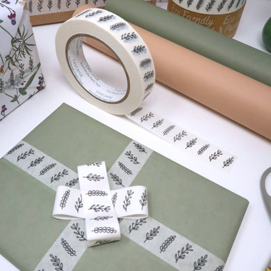 Roll of tape with leaf pattern on a white surface with gift wrap and scissors.