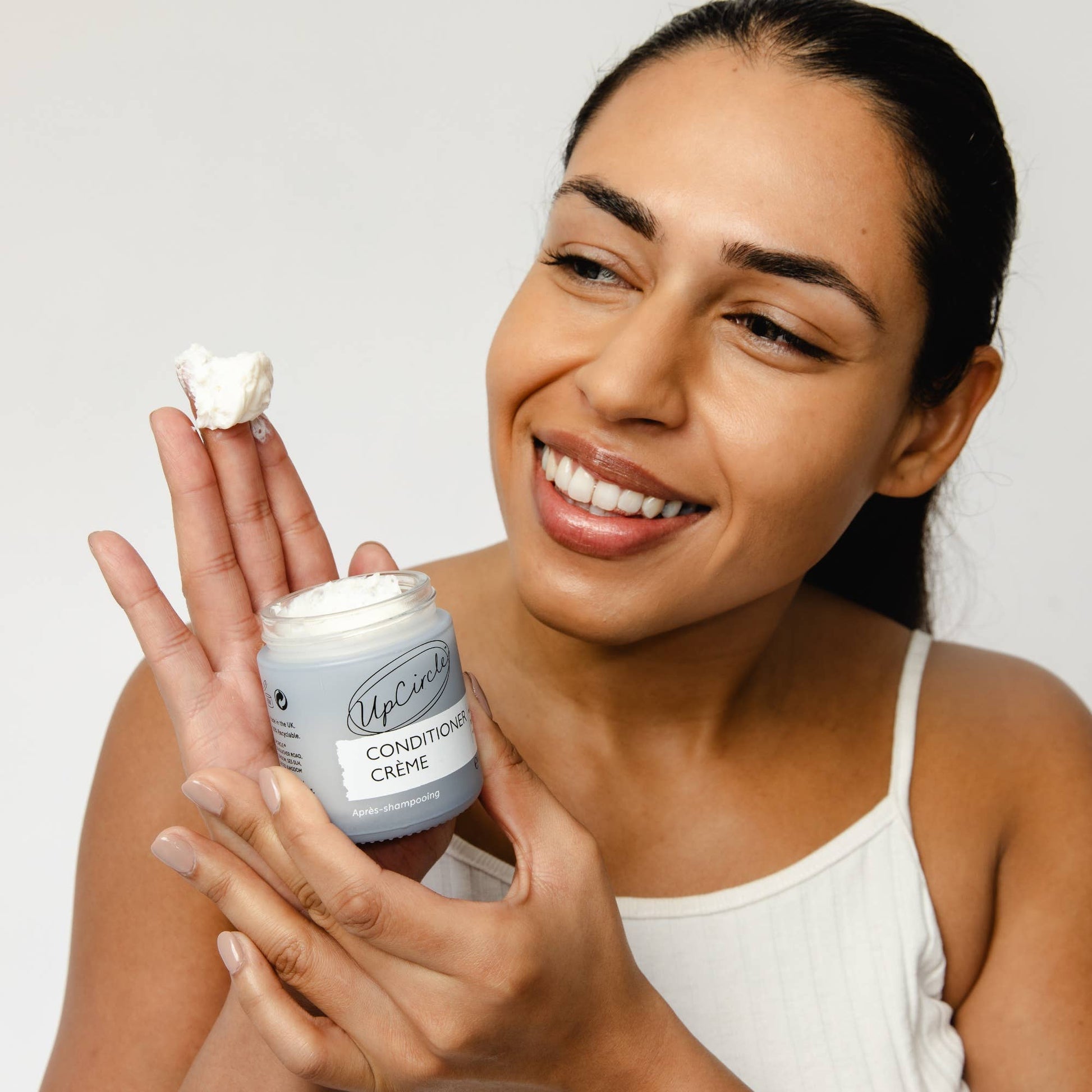 Woman holding a jar of UpCircle Condition Creme against a plain background