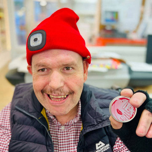 Man wearing a red beanie with a camera lens, holding a small round object, in an indoor setting.