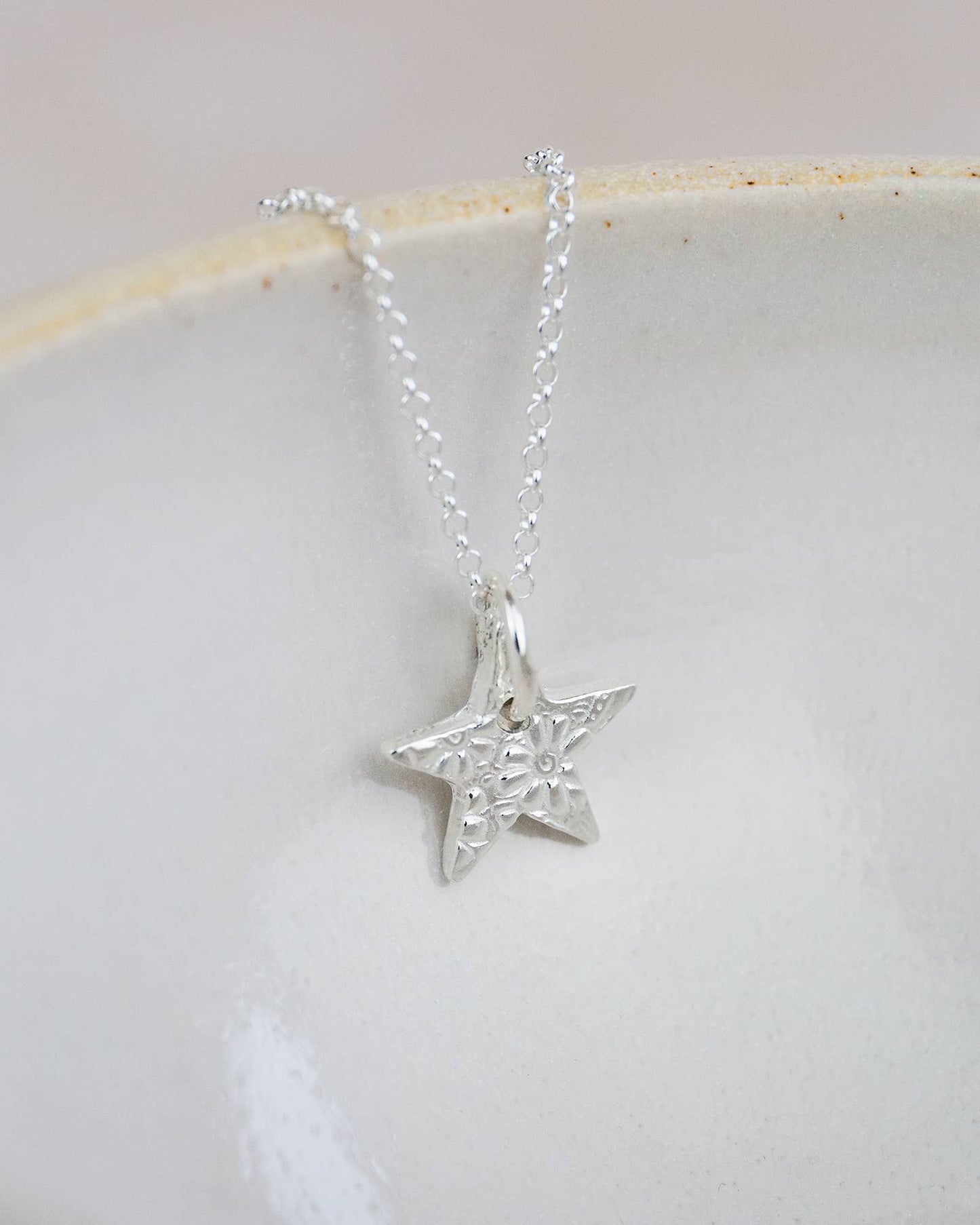Silver star-shaped pendant on a chain against a light background