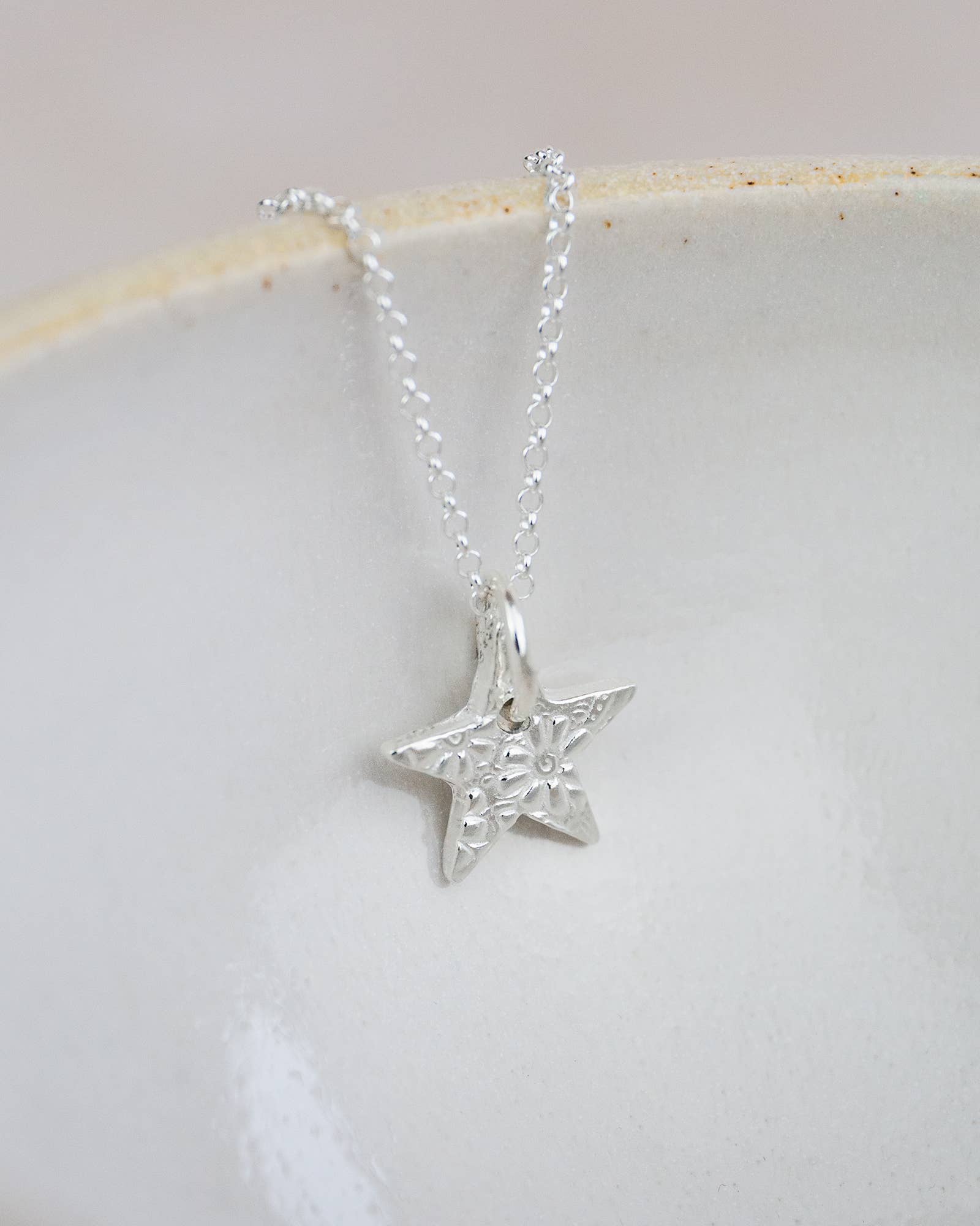 Silver star-shaped pendant on a chain against a light background