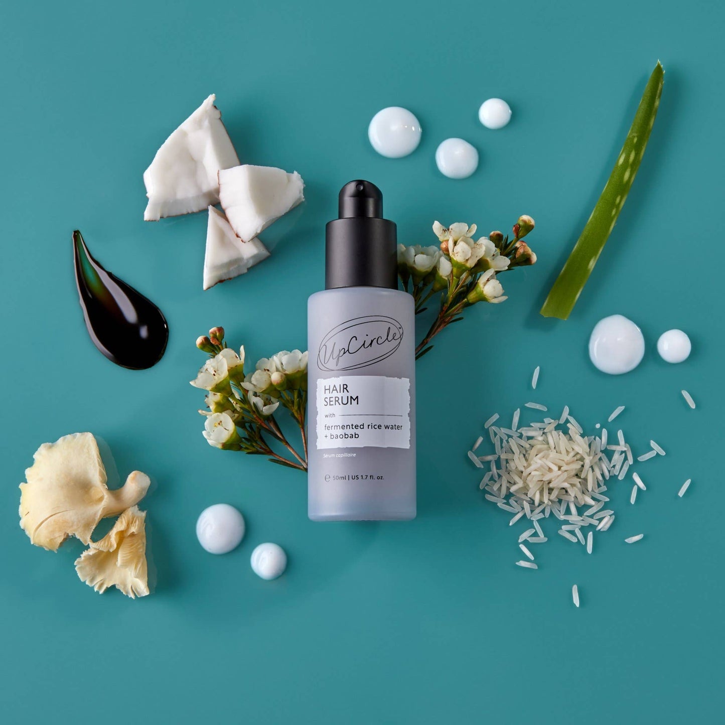 Hair serum bottle with natural ingredients on a teal background