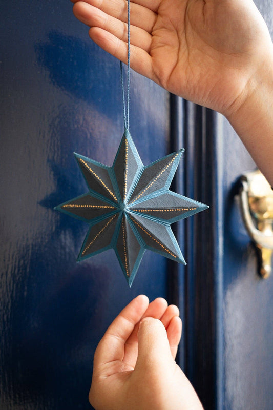 Hand holding a blue star-shaped ornament against a blue door.