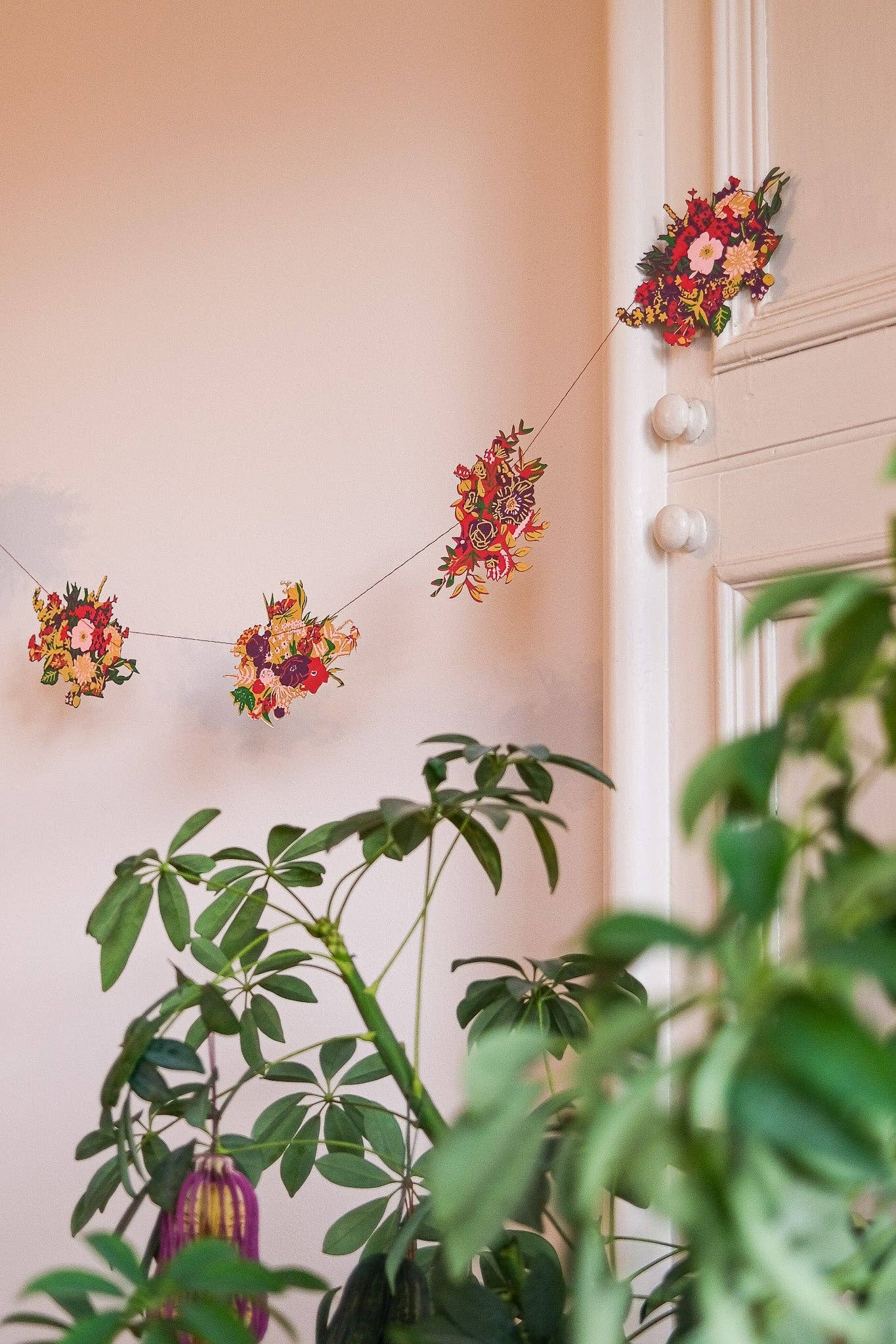 Decorative floral string lights hanging on a wall with plants in the foreground.