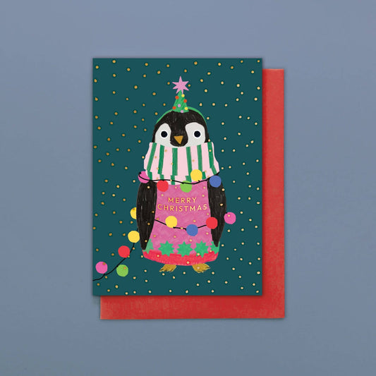 Christmas card with a penguin wearing a sweater and hat, surrounded by lights on a blue background.