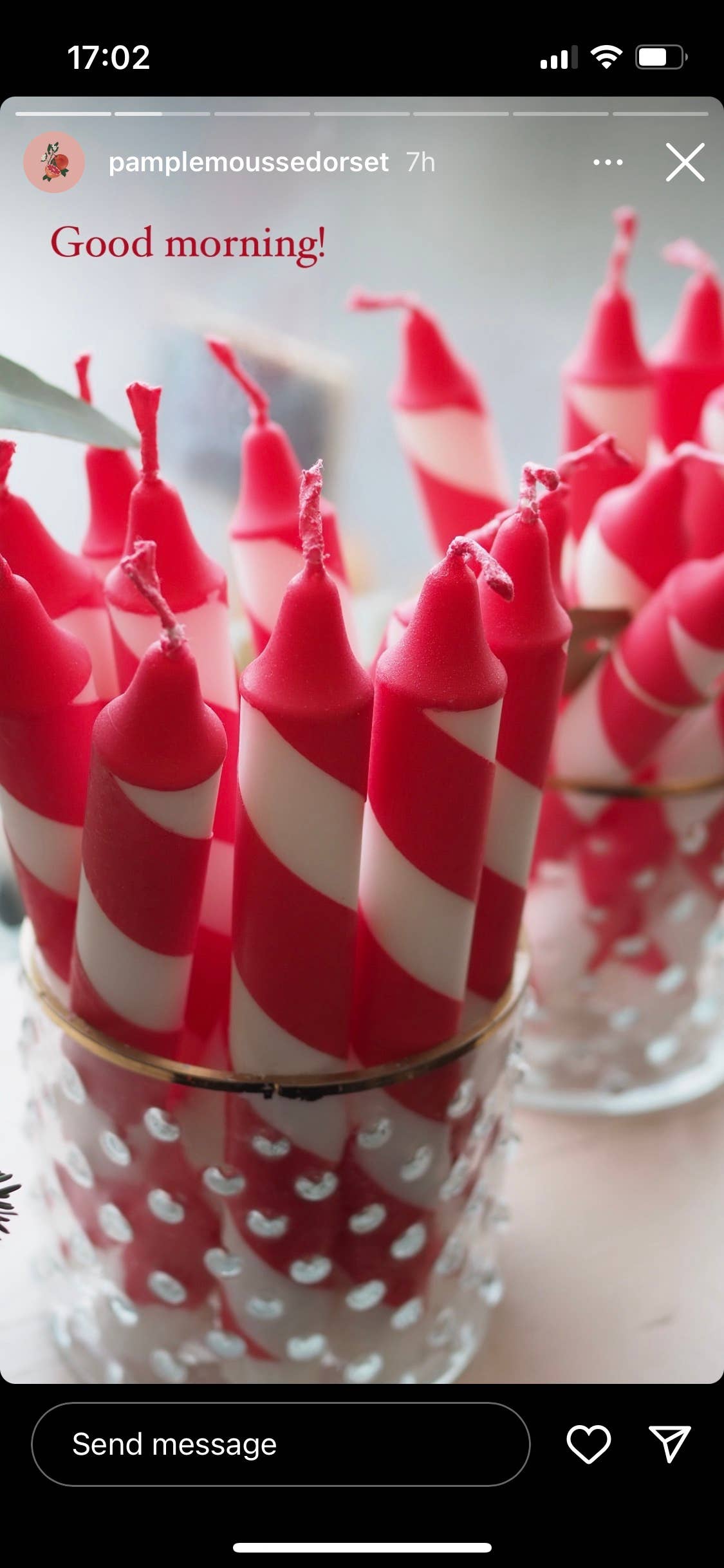 Red and white striped candles in a glass holder with a text overlay on a smartphone screen.
