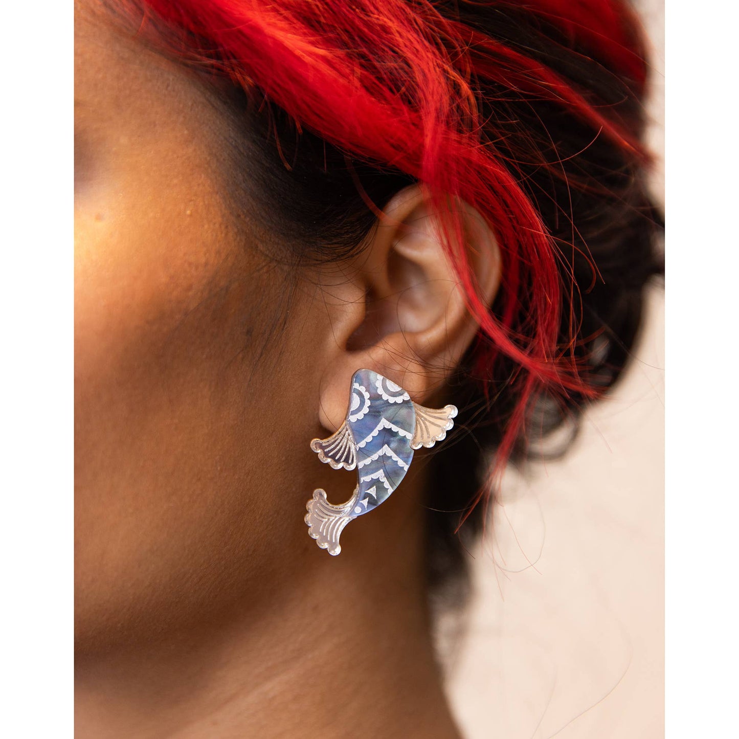Close-up of an ear wearing a fish-shaped earring with red hair.