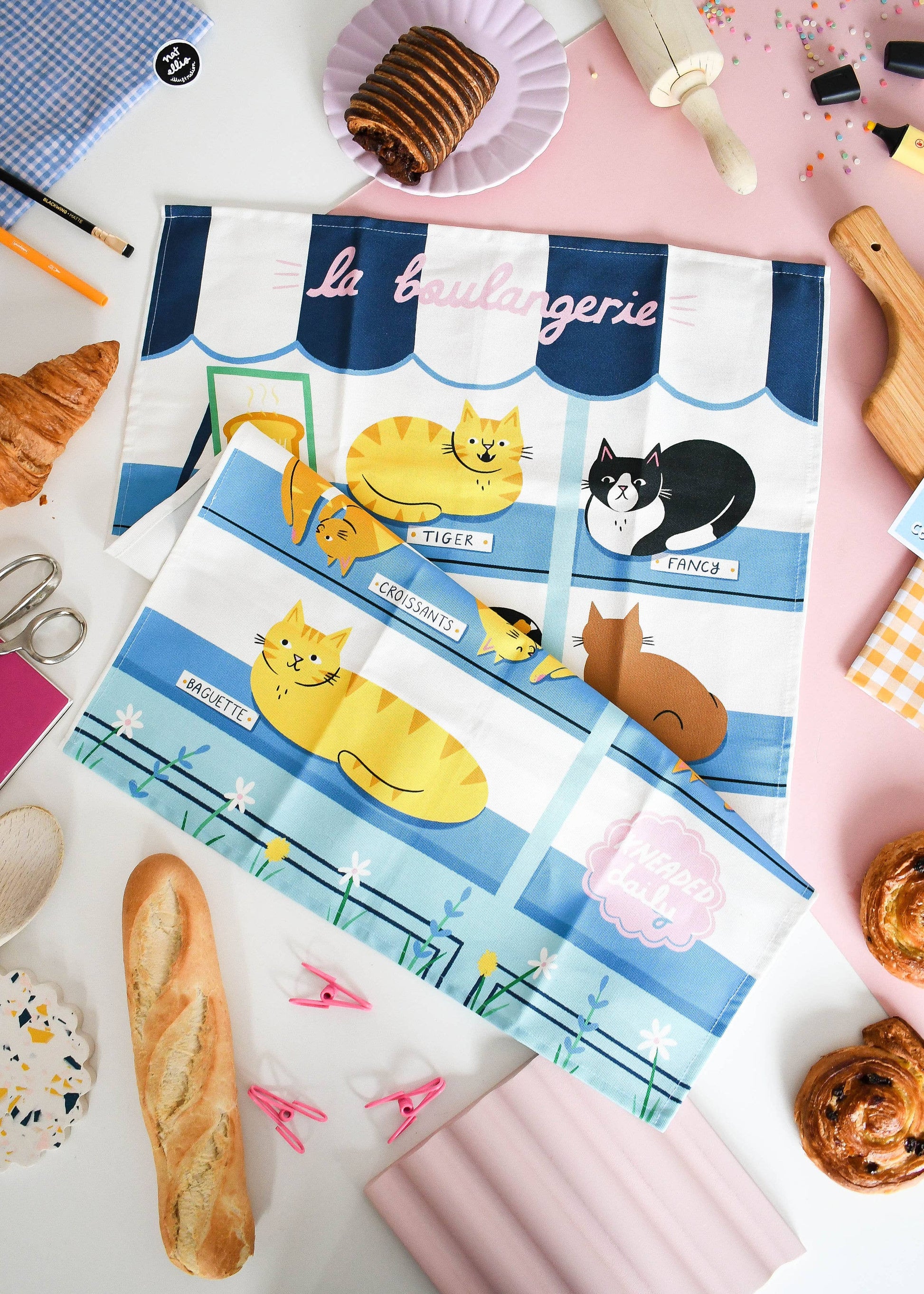 Set of placemats with cat illustrations on a table with pastries and kitchen items.
