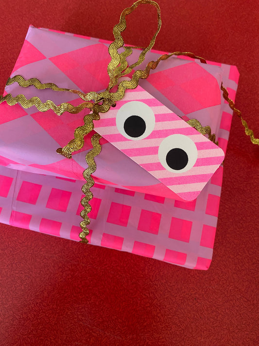 Pink checkered box with googly eyes and a gold ribbon on a red background