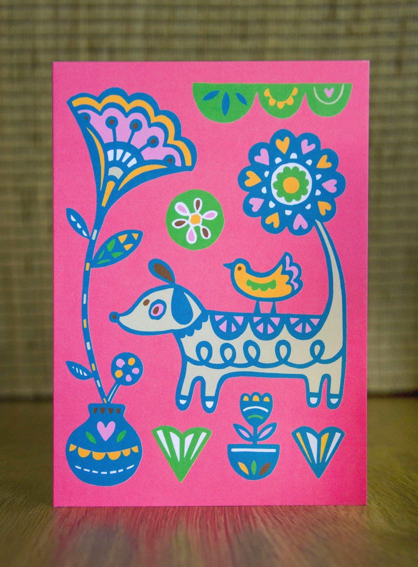 A colourful card featuring a dog, flowers, and bird on a pink background
