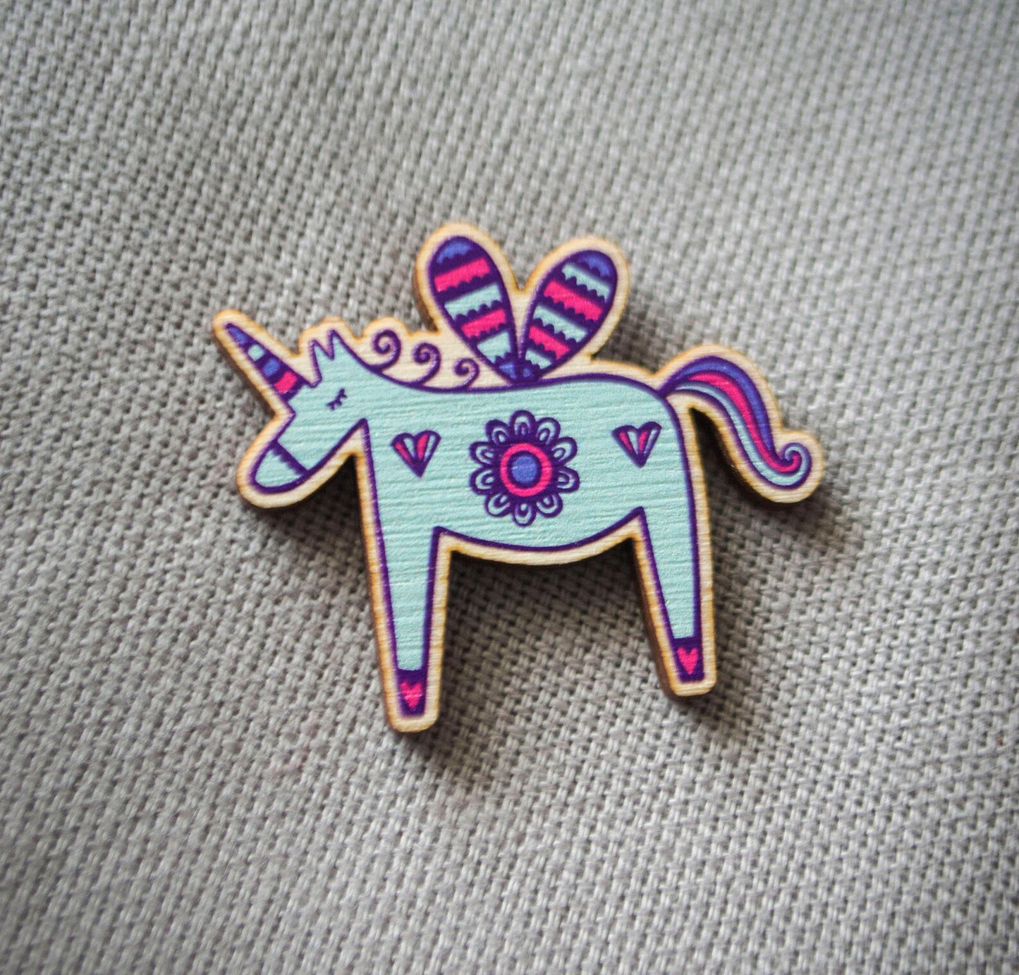A brightly painted wooden brooch of a unicorn.
