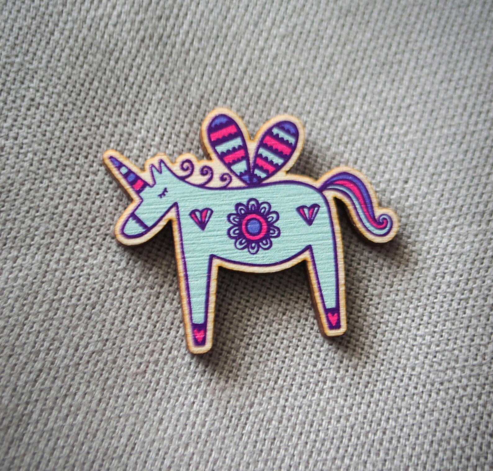 A brightly painted wooden brooch of a unicorn.