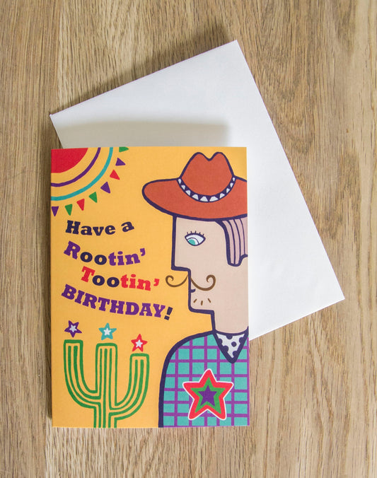 A card depicting a moustached cowboy next to a cactus, with a yellow background. To the left of the cowboy there is text that reads "Have a Rootin' Tooting' Birthday!"