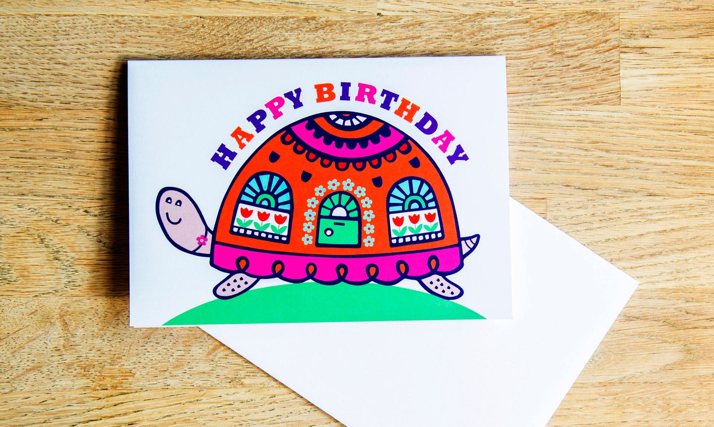 A card depicting a bright and colourful happy tortoise with a door and windows on its shell. Curved above the shell is the text "Happy Birthday".