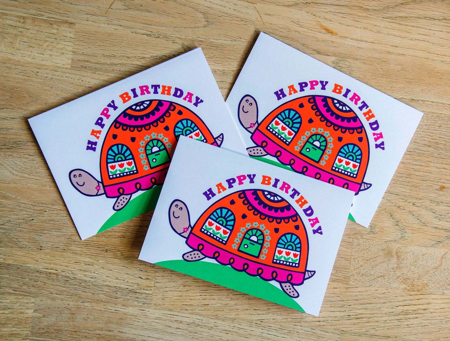 A card depicting a bright and colourful happy tortoise with a door and windows on its shell. Curved above the shell is the text "Happy Birthday".