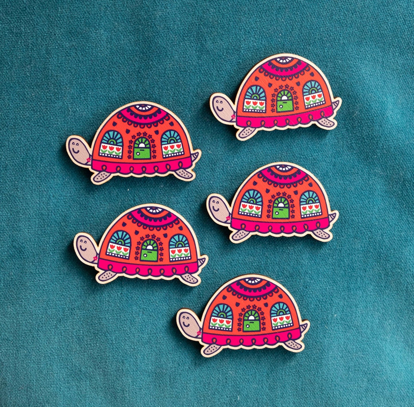 Five brightly painted wooden brooches of an art deco inspired tortoise with windows and a door on its shell.