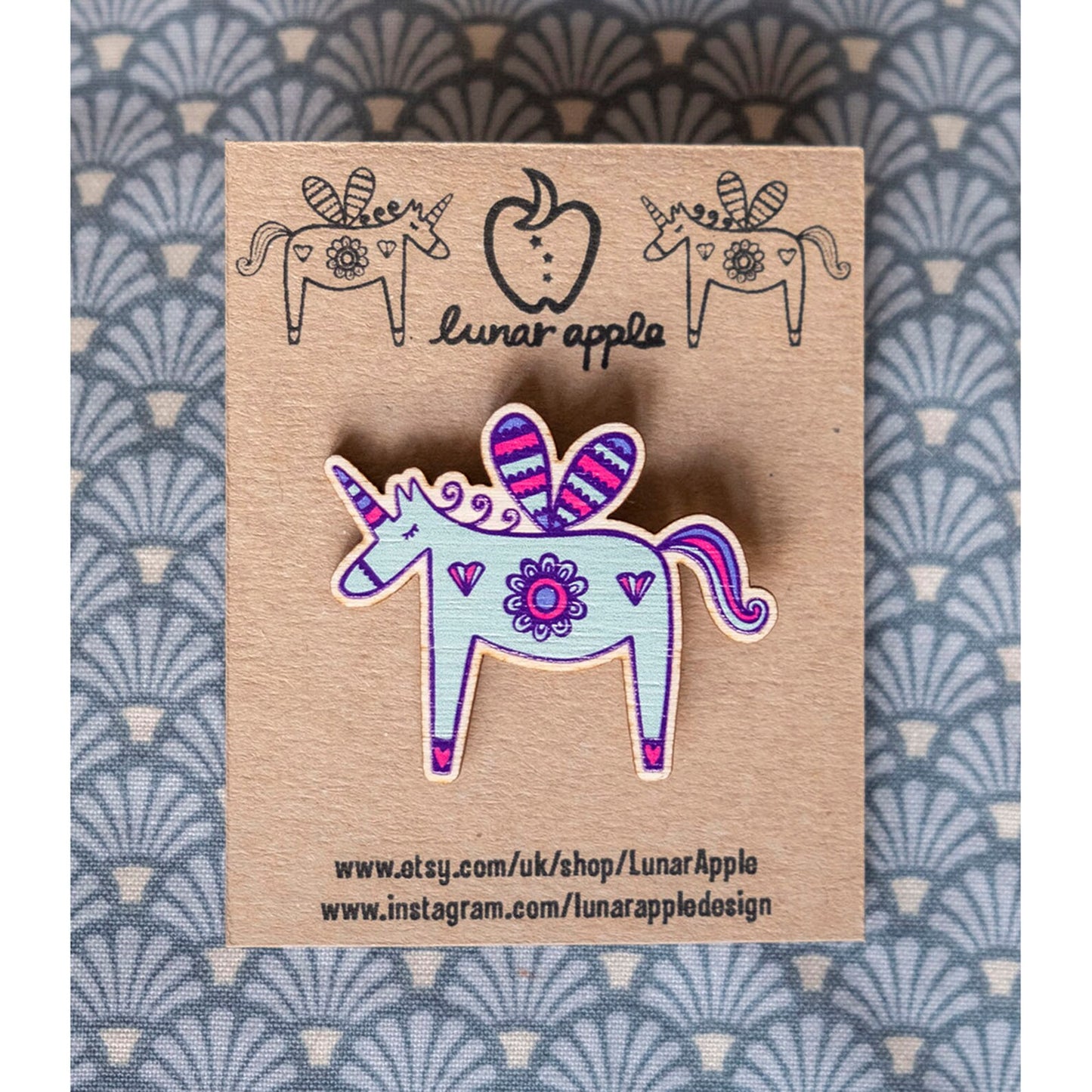 A brightly painted wooden brooch of a unicorn pinned to a brown card backing.