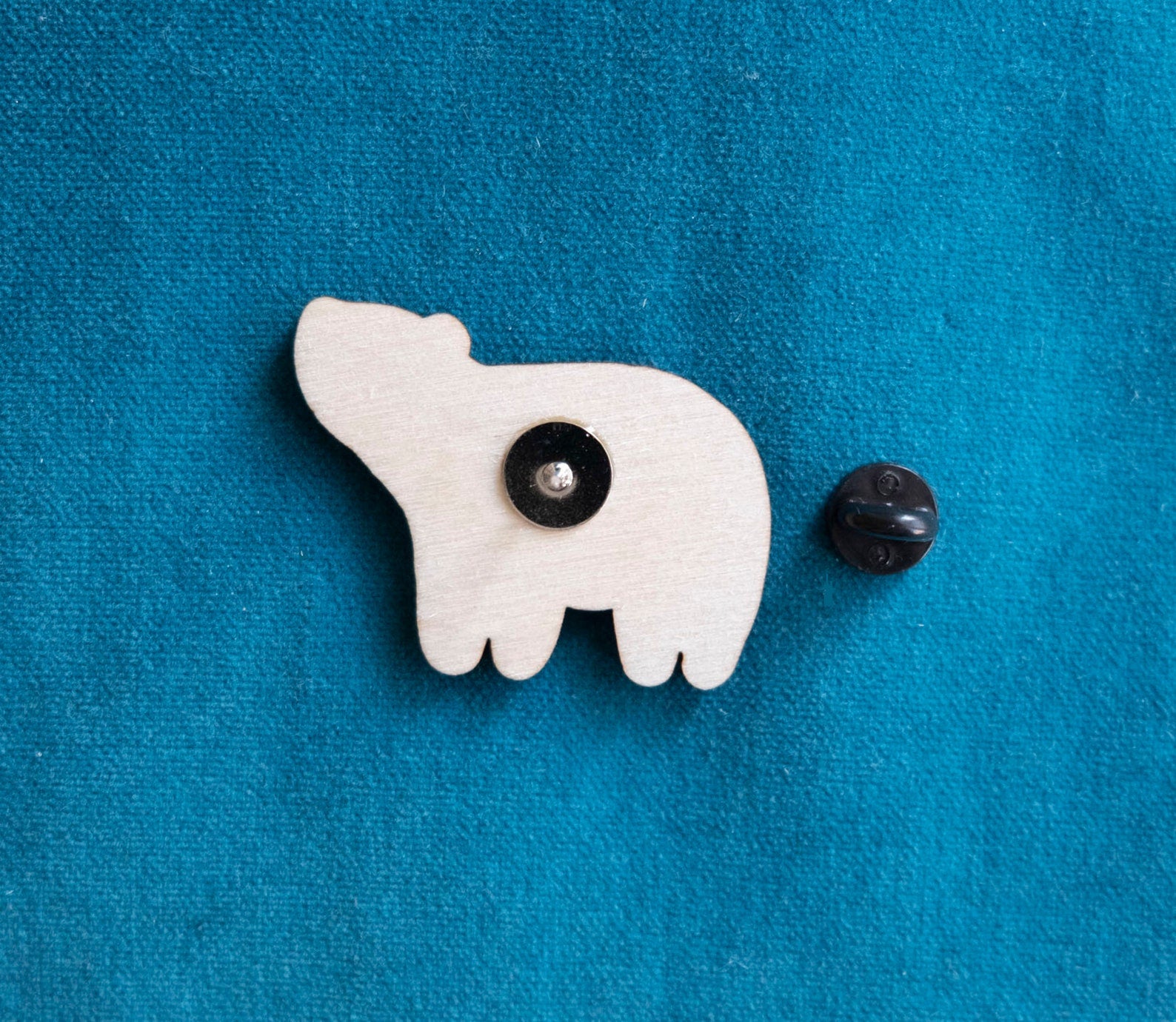 The back of a brightly painted wooden brooch of an art deco inspired smiling polar bear.