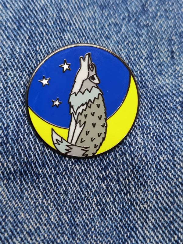 Enamel pin brooch with a howling wolf on a blue and yellow background with 3 small stars