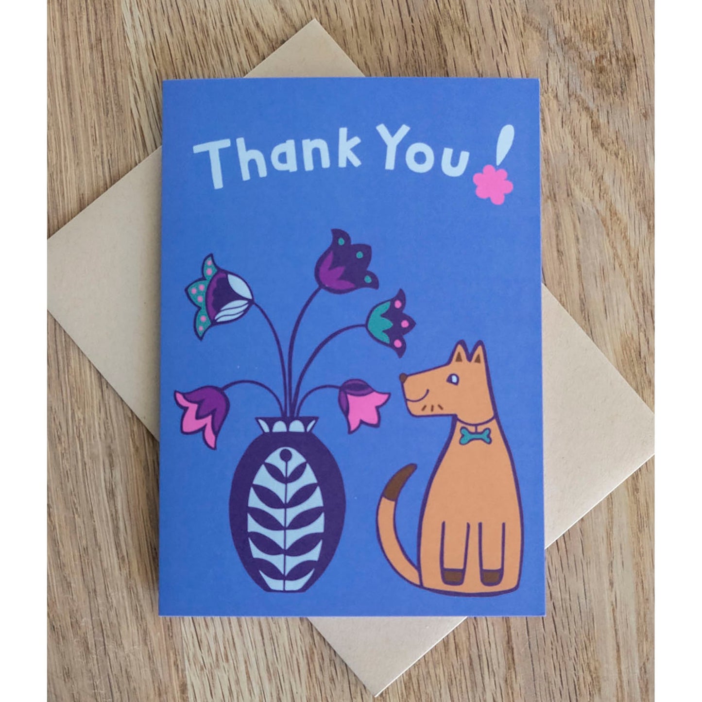 A blue thank you card with the phrase "Thank You!" on the top. Underneath there is a brown dog smiling and sat next to a flower vase.