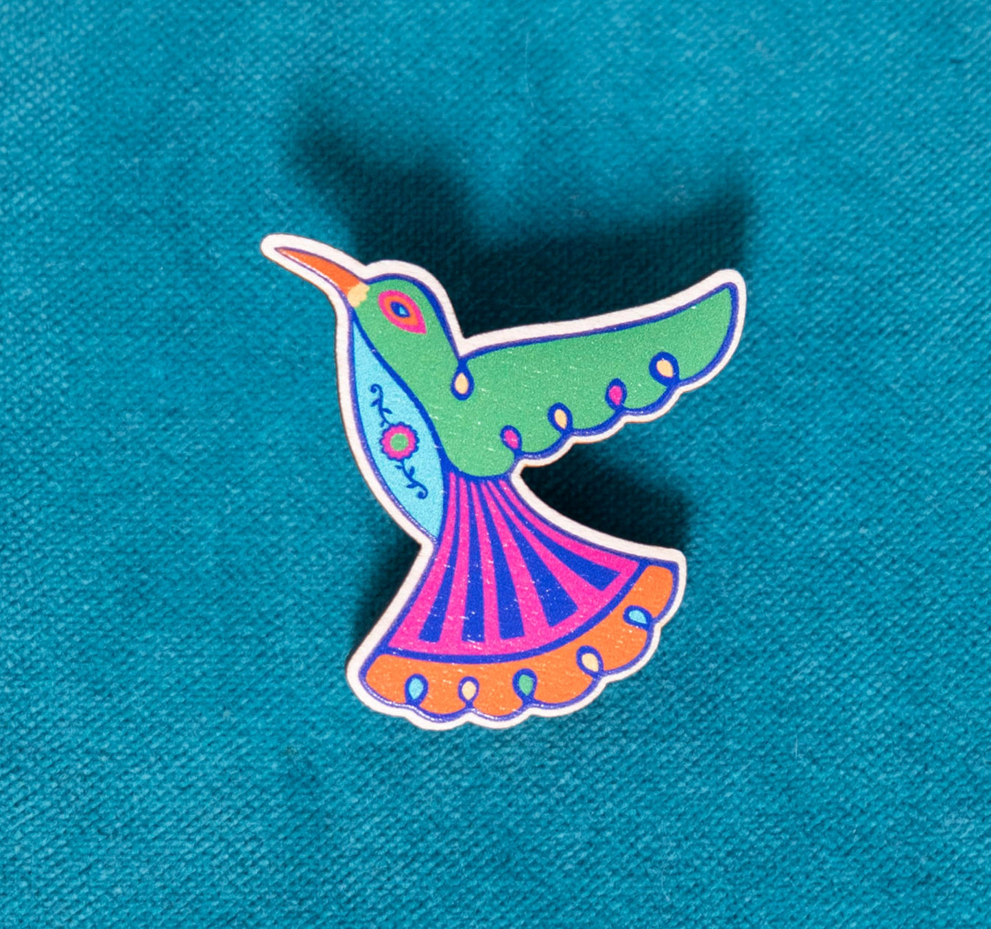 A brightly painted wooden brooch of an art deco inspired hummingbird.