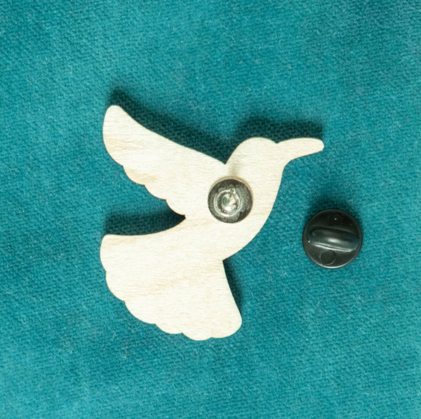 The back of a brightly painted wooden brooch of an art deco inspired hummingbird.