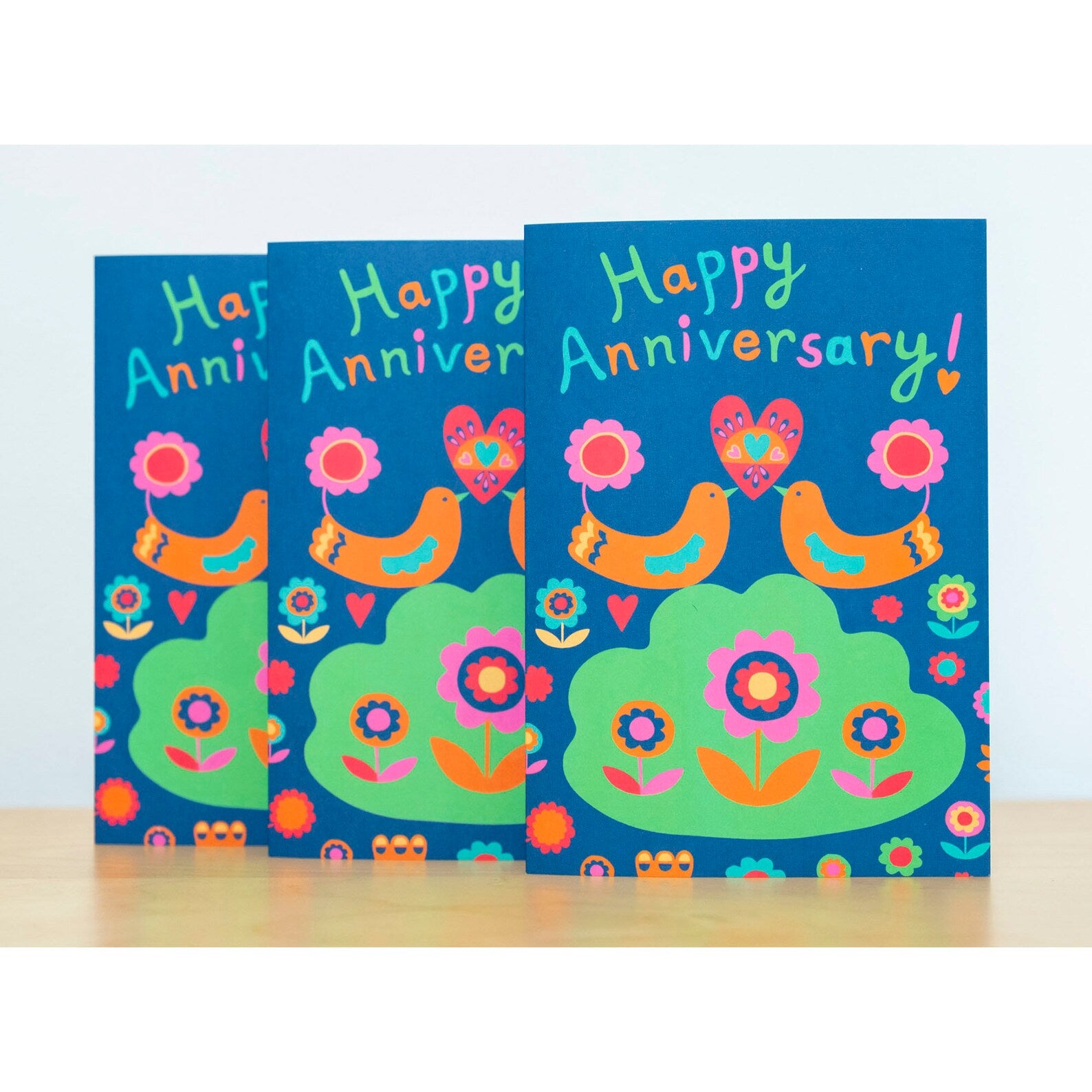 A card depicting two orange art deco birds holding up a heart together with their beaks. Above them reads the text "Happy Anniversary!"