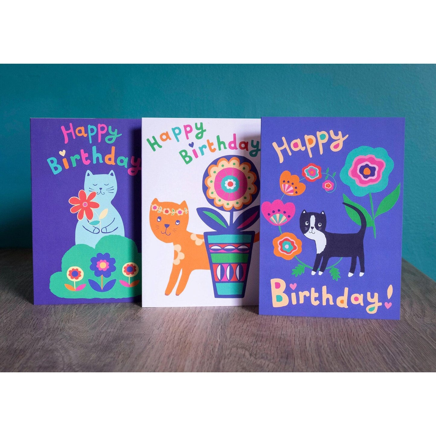 Three birthday card designs featuring cats with flowers.
