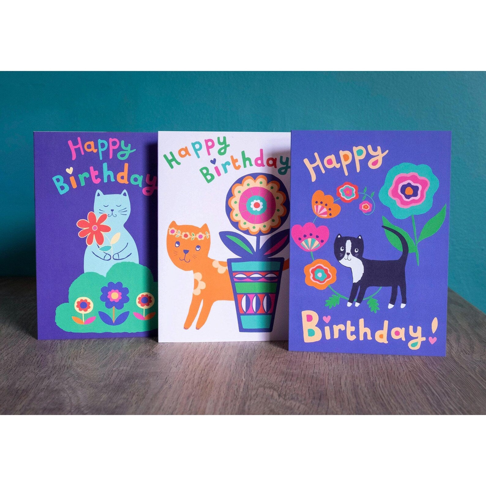 Three birthday card designs featuring cats with flowers.