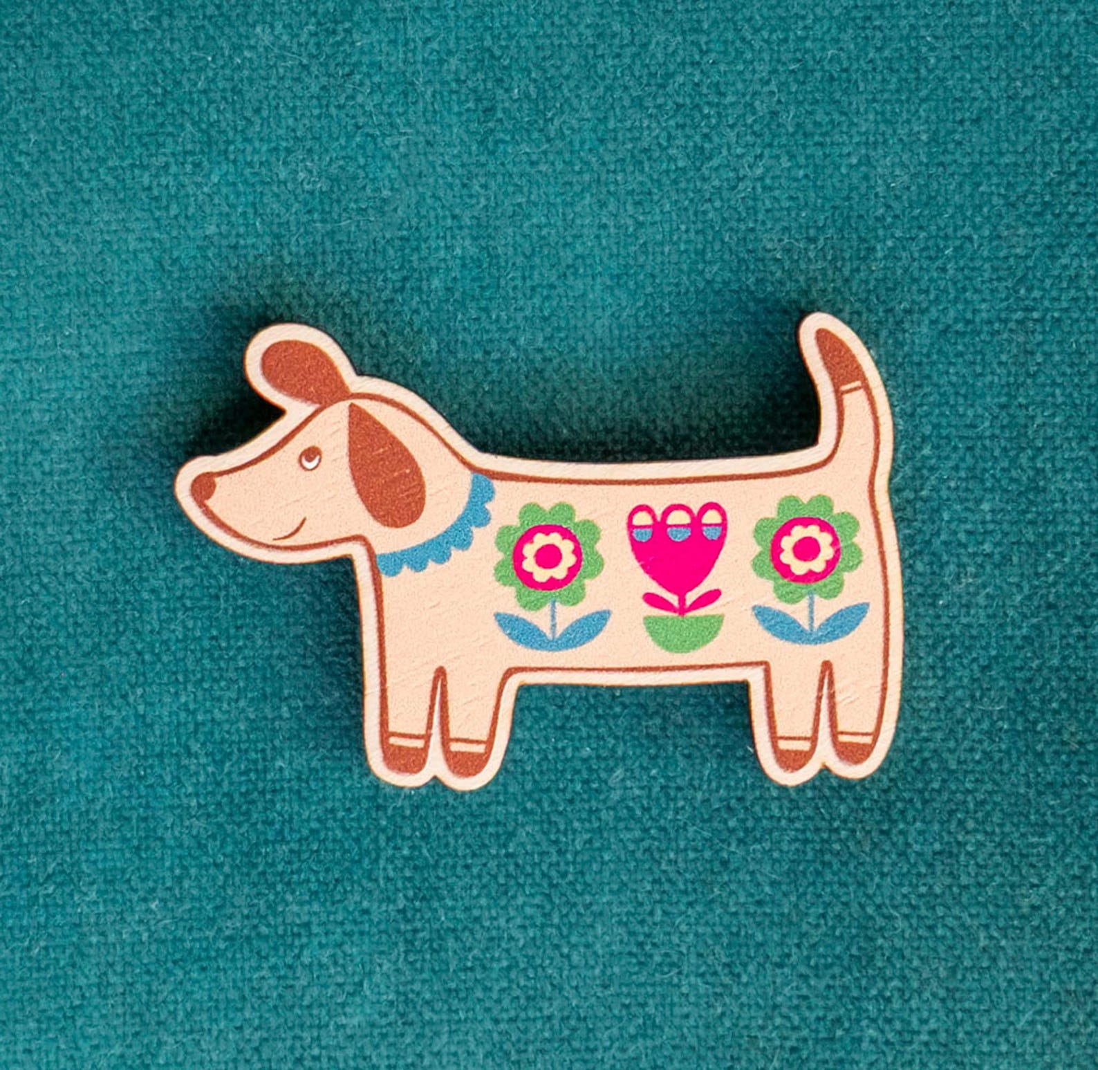 Decorative dog-shaped wooden brooch with floral patterns against a teal background
