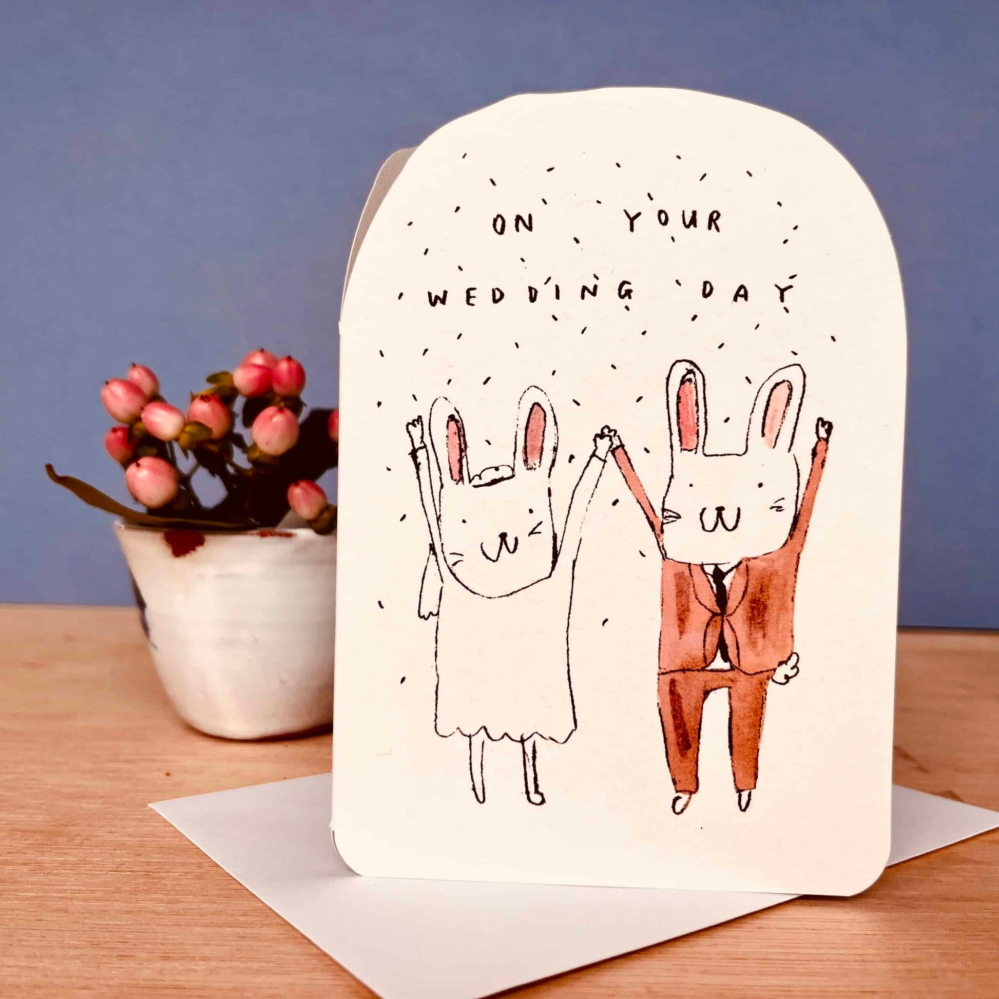 Wedding card with cartoon bunnies on a wooden surface with a plant in the background
