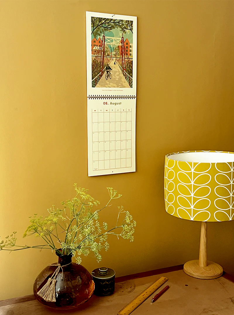 Calendar on a yellow wall with a lamp and vase in the foreground