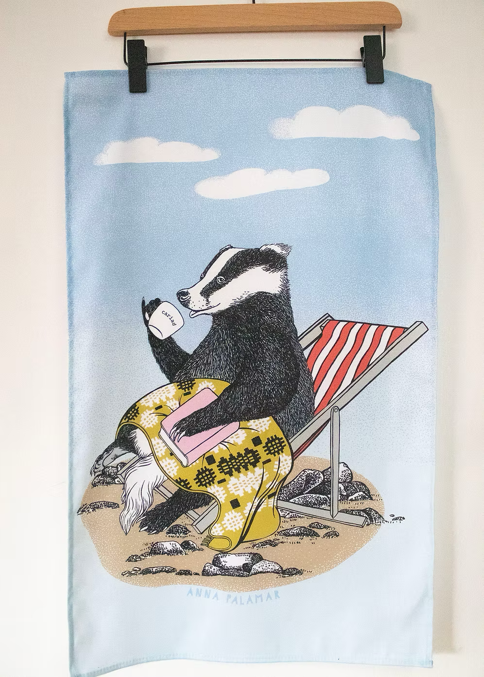 Towel with a badger design sitting on a beach chair under a blue sky with clouds.