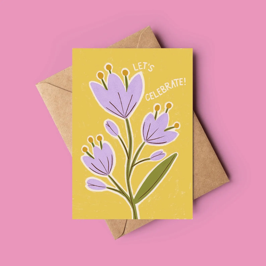 Greeting card with purple flowers and 'Let's Celebrate!' text on a yellow background, with a brown envelope.