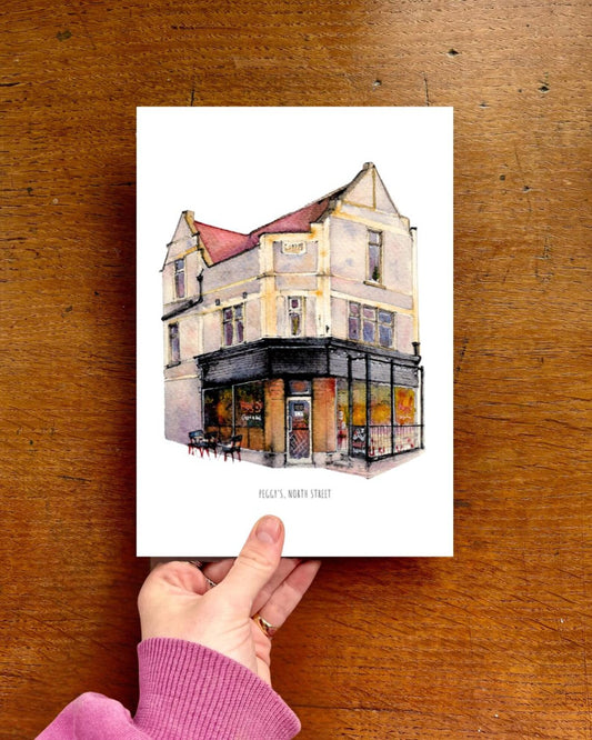Hand holding a card with a building illustration on a wooden surface