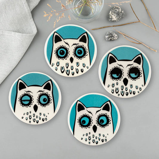 A set of four coasters with four different owl faces illustrations on a turquoise background