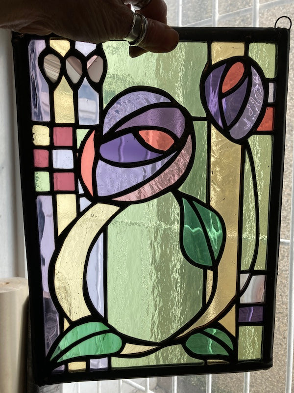 A Charles Rennie Mackintosh inspired stained glass hanging, with roses and leaves over a geometric design. Handmade by Dadswell Glass at Glass Designs in Bristol.