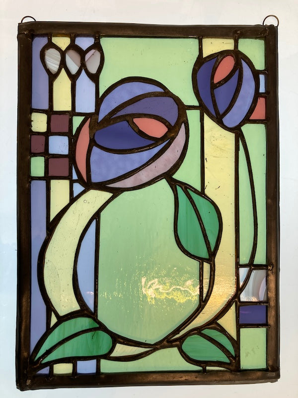 A Charles Rennie Mackintosh inspired stained glass hanging, with roses and leaves over a geometric design. Handmade by Dadswell Glass at Glass Designs in Bristol.