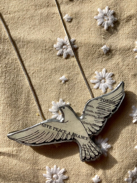 A dove on a 18 inch chain,  dove made from layered paper and steel then heavily laquered in resin.   The text Give Peace a Chance across one wing.