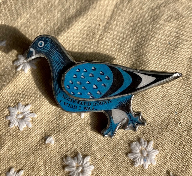 A Blue Pigeon with the text Homeward bound I wish I was on its body.  Made from layered paper and steel then sealed with resin.  A beautiful Brooch for  all pigeon lovers.