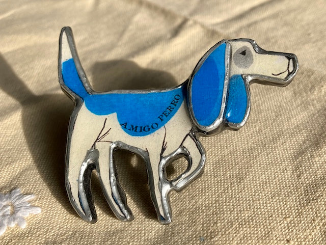 A Blue Beagle dog with the text Amigo Perro on its body.  Handmade brooch, materials used layered paper, metal and resin.