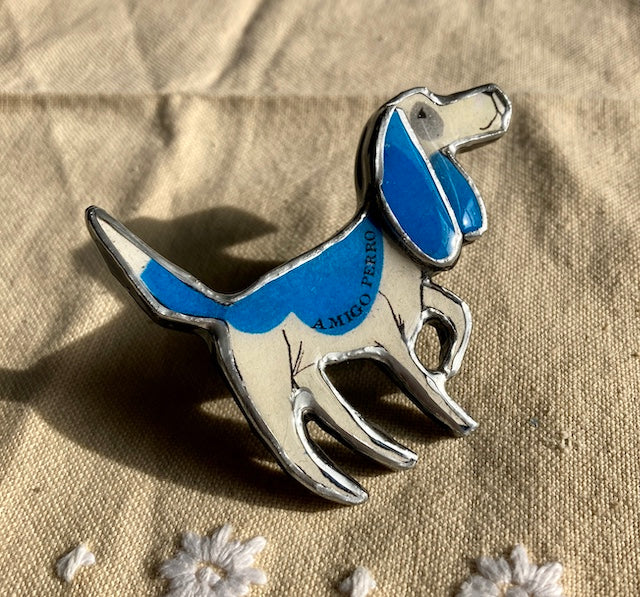 A Blue Beagle dog with the text Amigo Perro on its body. Handmade brooch, materials used layered paper, metal and resin.