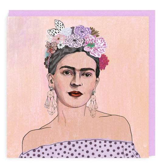 Card with hand illustrated portrait of Frida Kahlo in shoulderless dress and flowers in her hair. Background is pale pink.